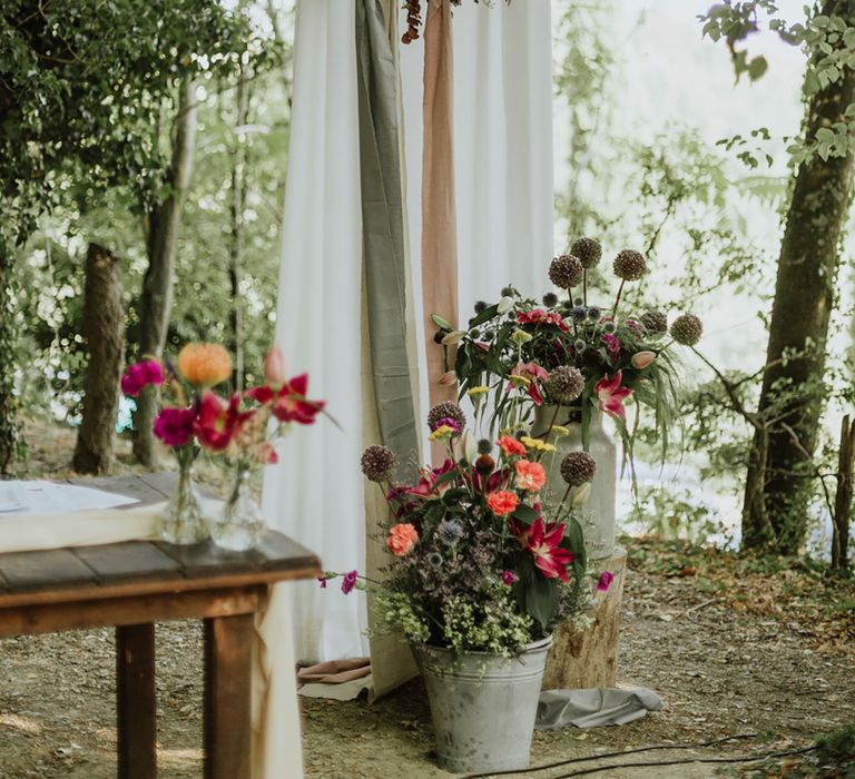 Woodland wedding with floral hoop decor, greenery, and pots of pink flowers with echinops