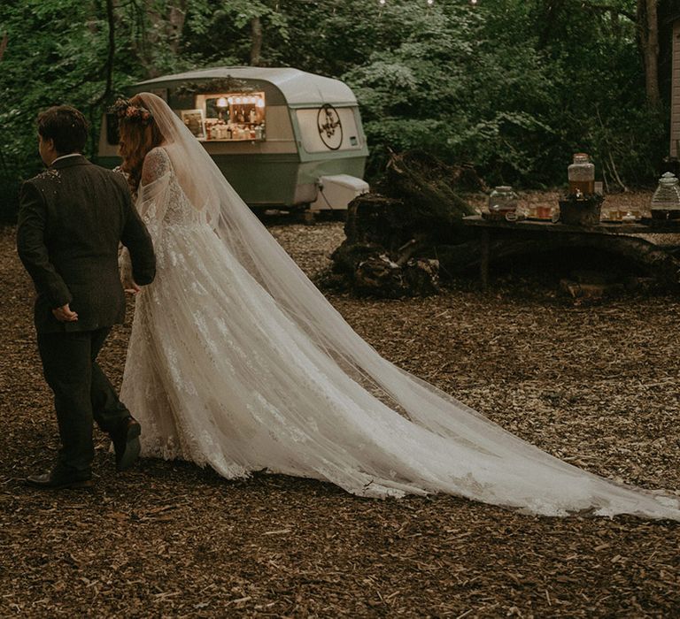 Bride in off the shoulder floral lace wedding dress walking with the groom at their woodland wedding at Lila's Wood