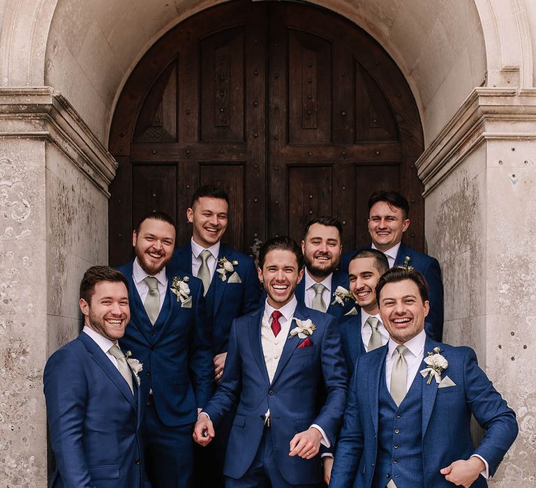 Groom and groomsmen in matching blue suits with the groomsmen wearing sage green ties and the groom wearing a red tie