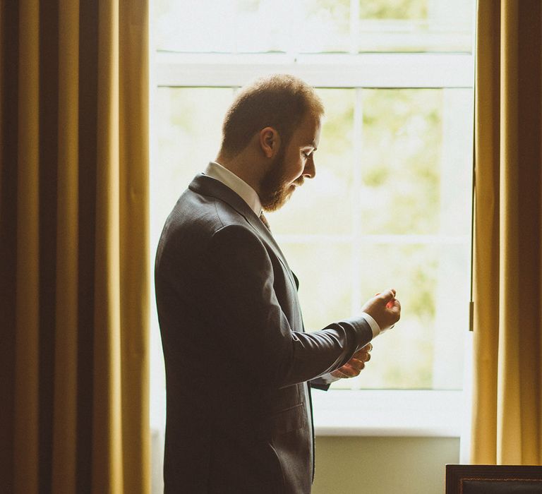 Groom in blue suit getting ready for the wedding day putting on cufflinks