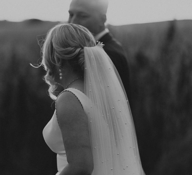 Bride wearing pearl accessories including a pearl wedding veil walking hand in hand with the groom 