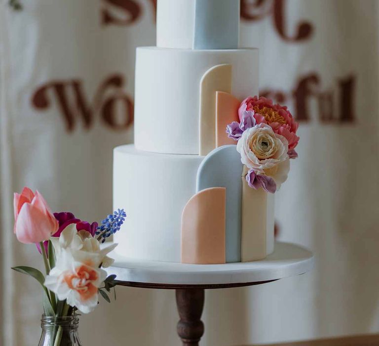 Three tiered buttercream wedding cake with pastel icing and garden rose decorations on stone cake stand 