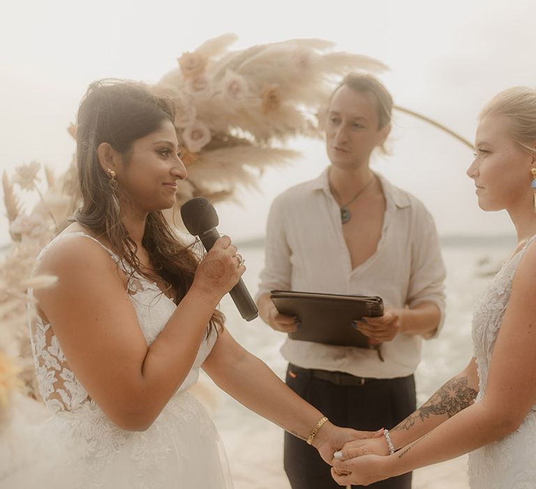 LGBTQIA+ wedding with two brides exchanging vows at coastal wedding with pampas grass moon gate