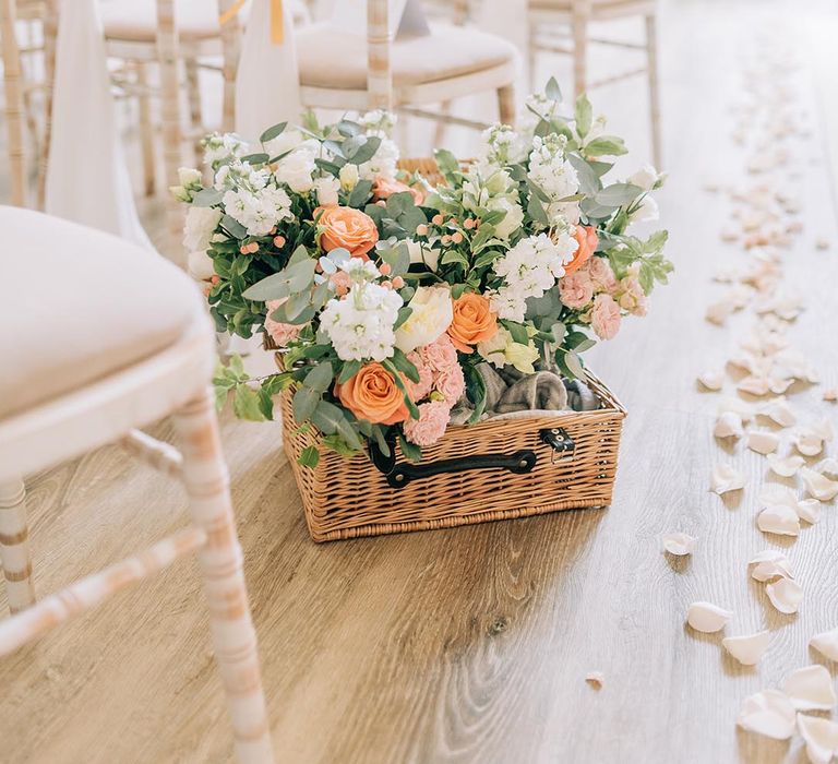 Wicker basket full of neutral wedding flowers with pops of peach and coral for the aisle decorations 