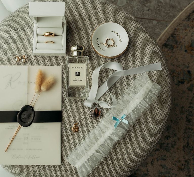 Monochrome bridall accessories including Jo Malone London wedding perfume, a bridal garter, gold wedding ring, wedding invitation, pearl earrings and a sentimental locket