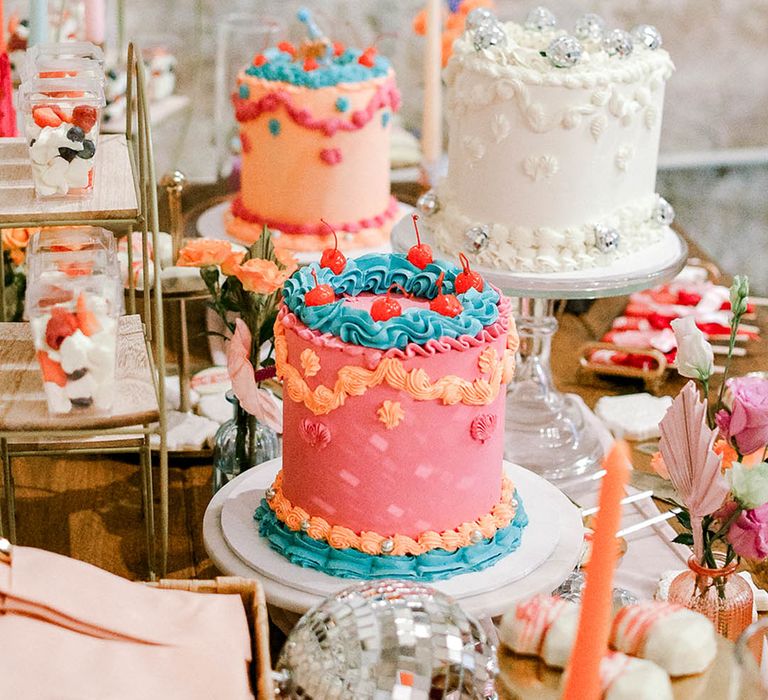 Retro style single tier wedding cakes with pink and blue bright icing with heart shaped white retro cake decorated with disco balls 