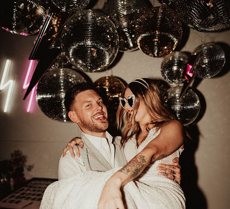 Pink and white lightning neon signage with gold and silver disco balls featuring the bride and groom in light coloured outfits 