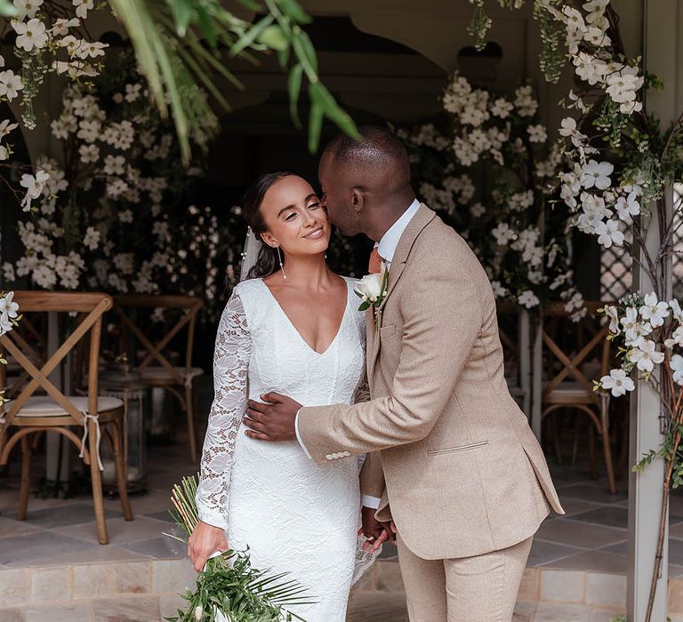 Bride in long sleeve boho lace wedding dress holding white wedding bouquet with the groom in a beige suit 