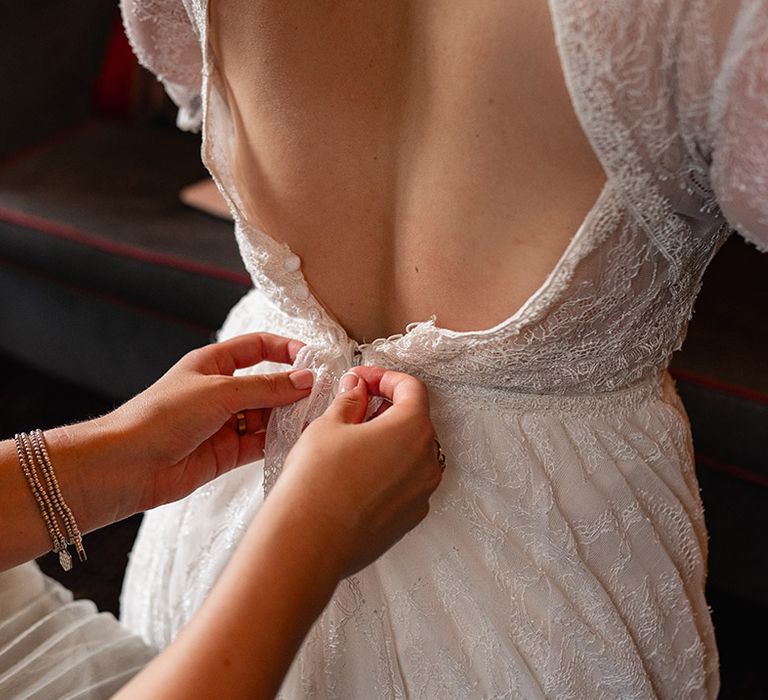 Bridesmaid helps the bride into her wedding dress as they get ready 