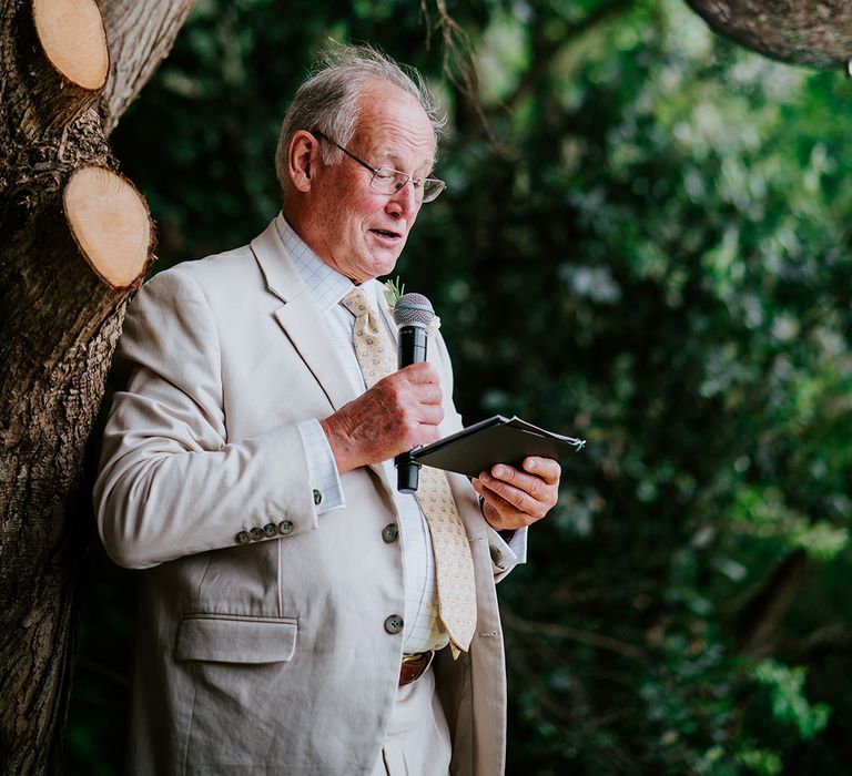 Father of the bride reads wedding speech at outdoor ceremony 