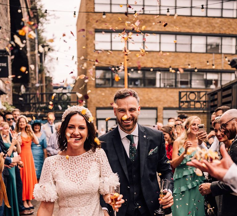 Bride in floral print wedding dress with the groom in a three piece navy suit with confetti 