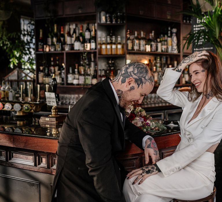 Tattooed bride and groom sitting at the bar of their pub wedding 