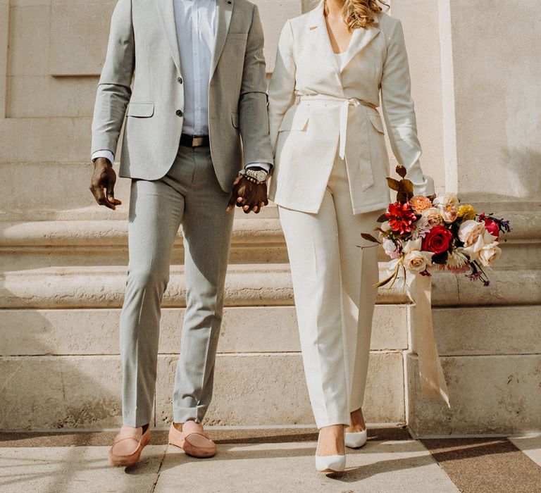 Stylish bride and groom in grey and ivory suits with colourful fashion and footwear