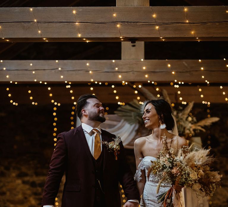 Smiling bride holding pampas grass bouquet walking down the aisle holding hands with groom