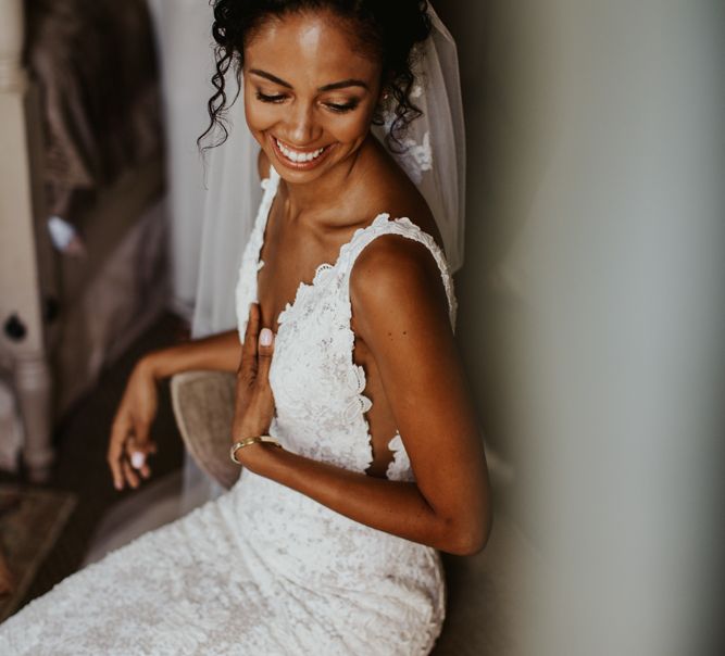 A bride shows off a great example of hairstyles for Black brides with a curly low bun. She wears a v neck dress and laughs.