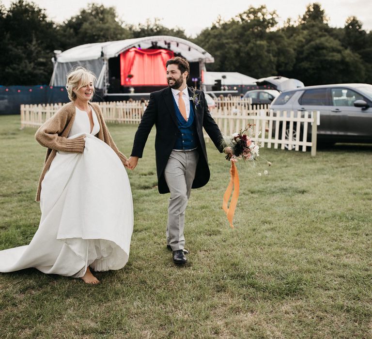 Bride in a Jesus Peiro wedding dress and cardigan holding hands with her groom in a classic morning suit 