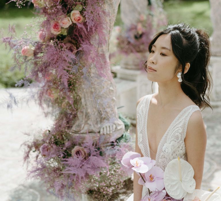 Bride sits with dark haired pulled into a high ponytail and wears large pearl drop earrings