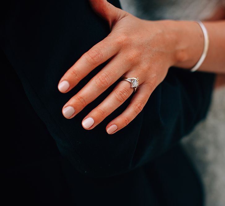 Bride holding grooms arm showing her engagement and wedding ring with pink nails