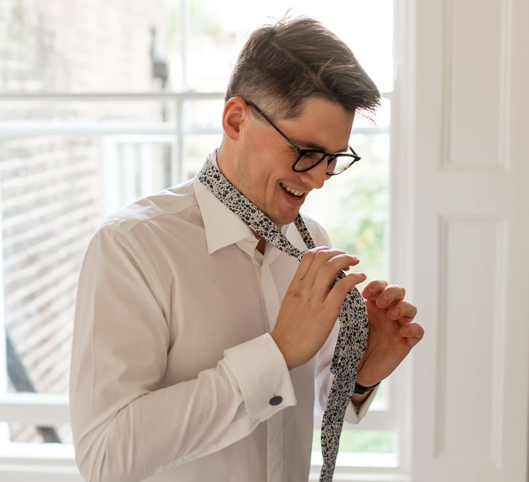 Groom putting on a navy and white Liberty print tie 