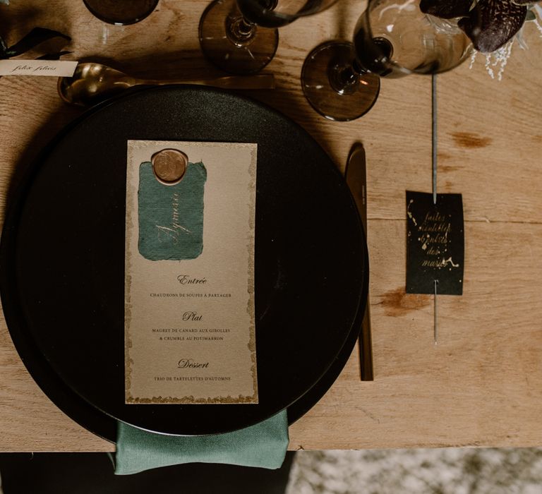 Place setting with black charger plate, gold cutlery and menu card