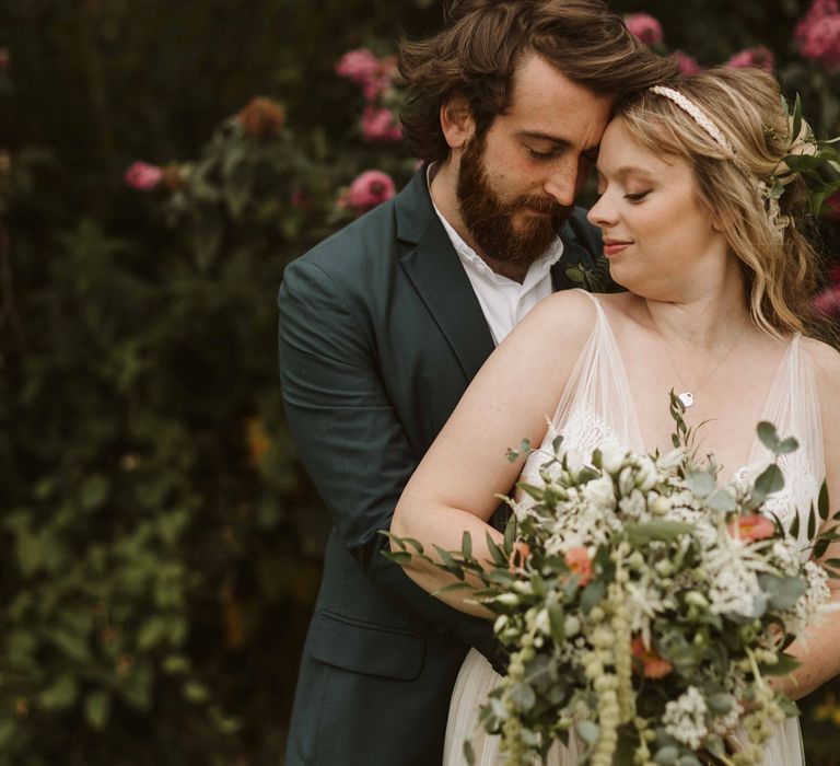 Groom embraces bride whilst bride holds floral bouquet