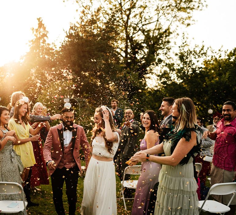 Bride & groom walk through confetti together during golden hour after wedding ceremony