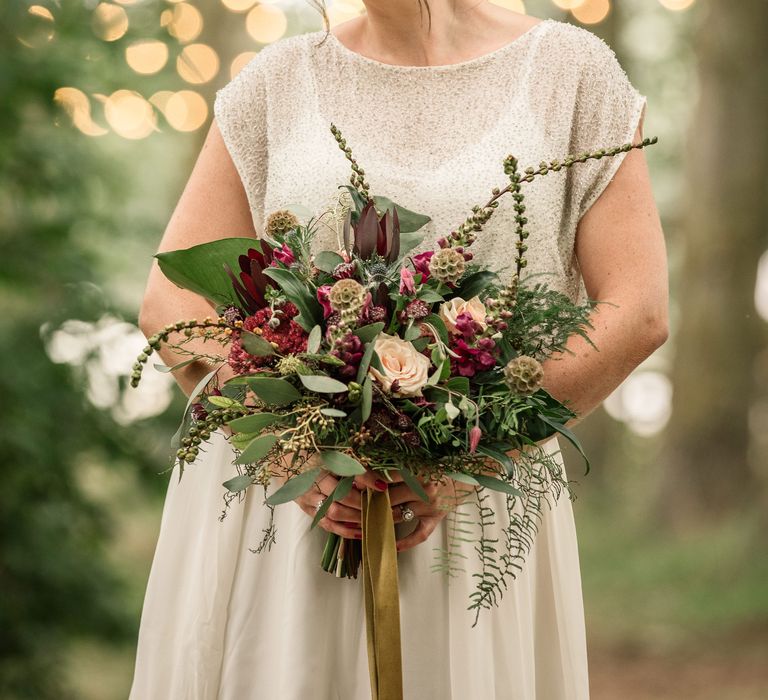 Bride carries floral bouquet and wears her hair in low updo with curls around face