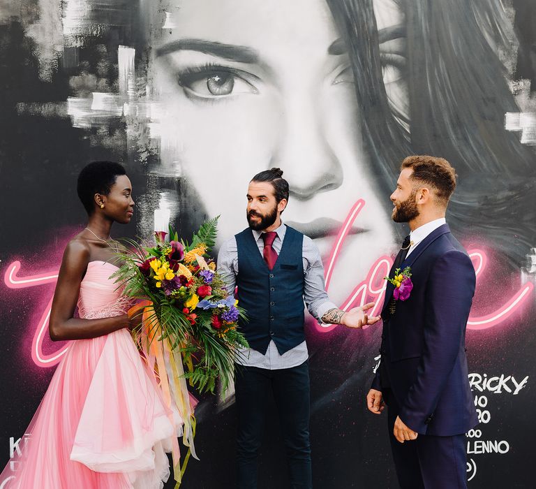 Bride holds colourful bouquet as she marries groom in front of black & white graffiti mural