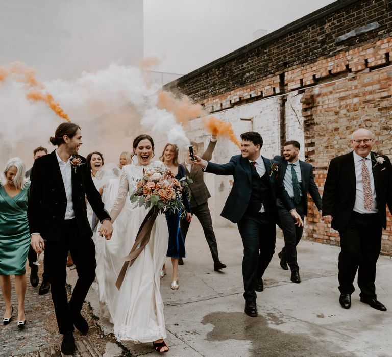 Bride and groom celebrating with wedding party with orange smoke canons outdoors 