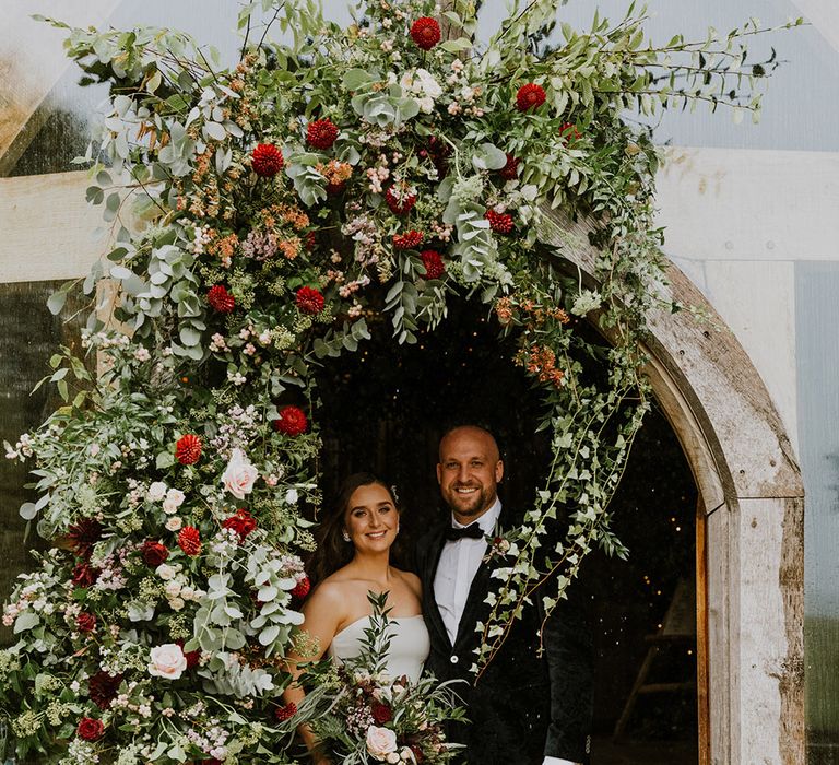 Bride and groom standing at the wedding venue entrance surrounded by natural wedding flowers and foliage