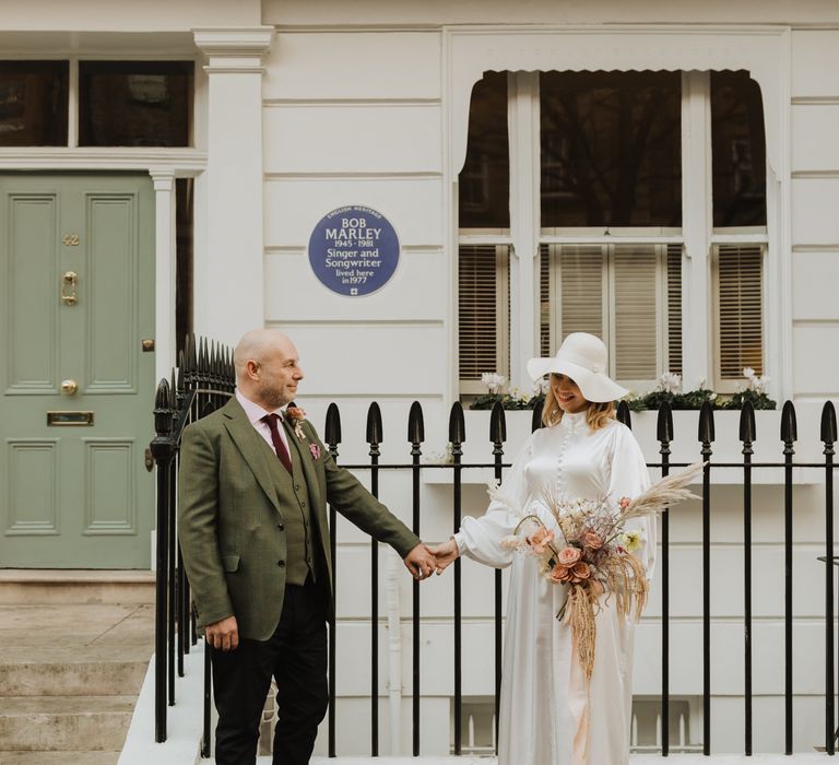 Bride & groom stand in front of house in Chelsea holding hands