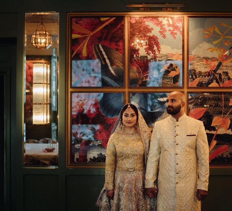 Bengali bride and groom standing in front of an Art-Deco artwork at The Ivy, Birmingham 