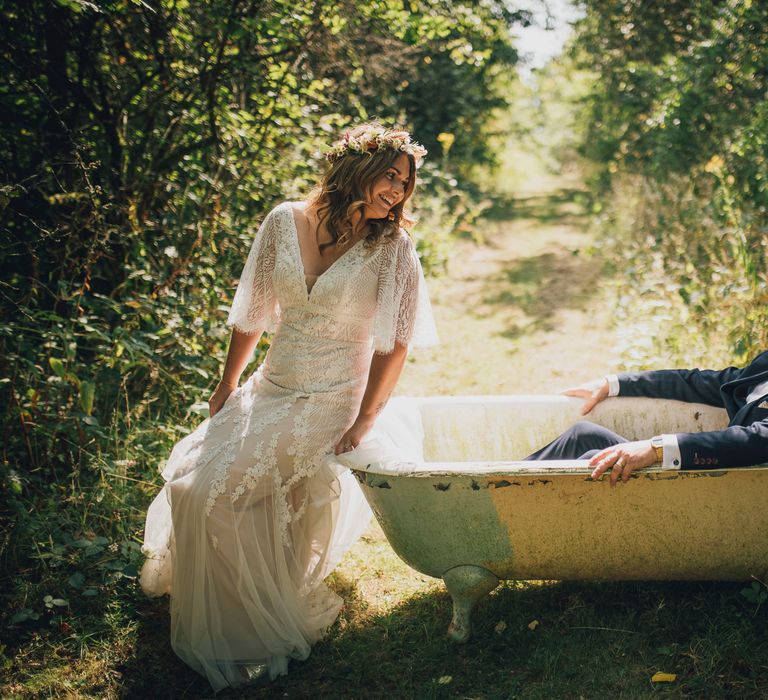 Bride sits at the side of roll top bathtub whilst the groom lays down within 