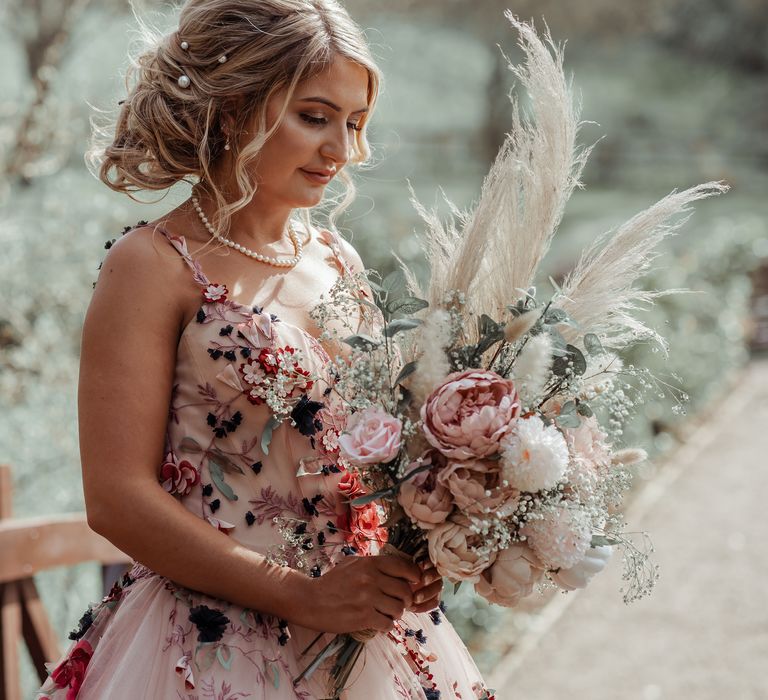 Bride stands with floral bouquet filled with blush pink peonies and pampas grass