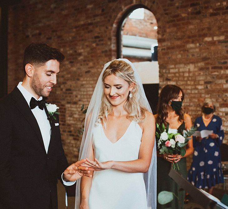 Groom in a black tuxedo with white rose buttonhole looking at his brides wedding ring at the ceremony altar 