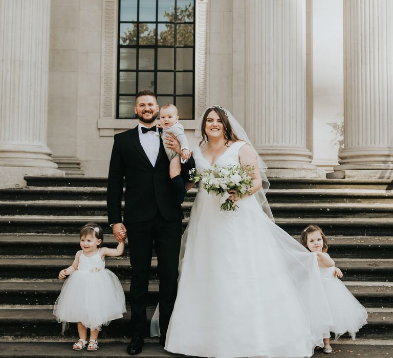 Bride & groom stand with their children on the steps of Old Marylebone Town Hall, as flower girls wear tulle skirt dresses