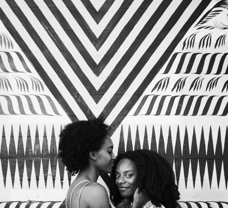 Black and white portrait of two brides embracing in front of a graffiti wall during their engagement session