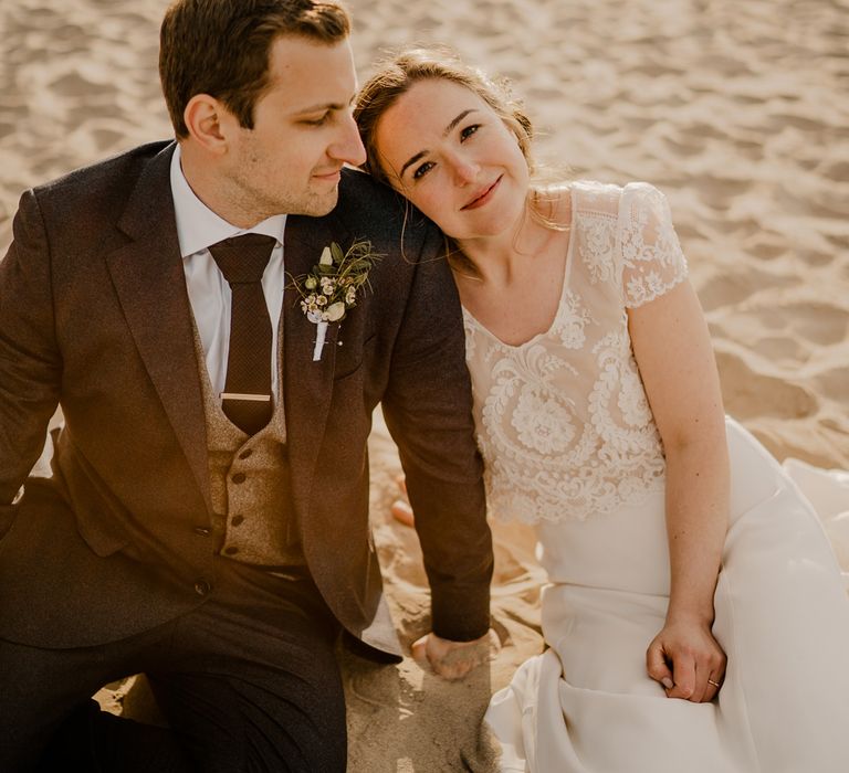 Smiling bride in lace top capped sleeve wedding dress sits holding hands of groom after Dunluce Castle wedding