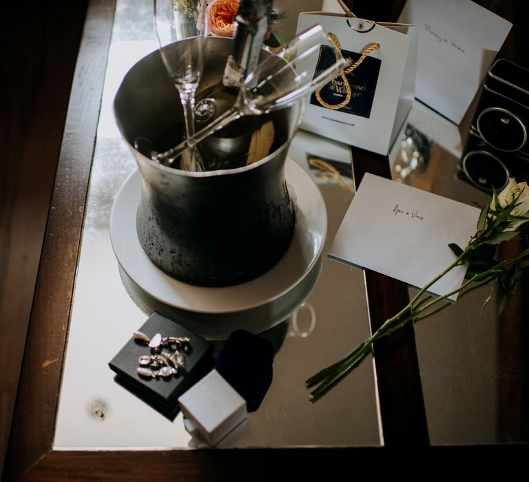 Champagne in ice bucket with two classes, white roses, vintage camera and assorted wedding items on glass table at Harrogate wedding