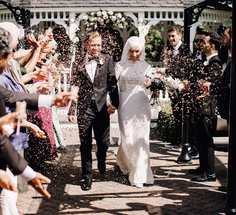 Bride and groom walk through wedding guests throwing confetti