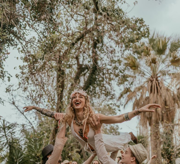 Wedding guests dance and lift up girl as they walk through the countryside of Sicily for hippie wedding