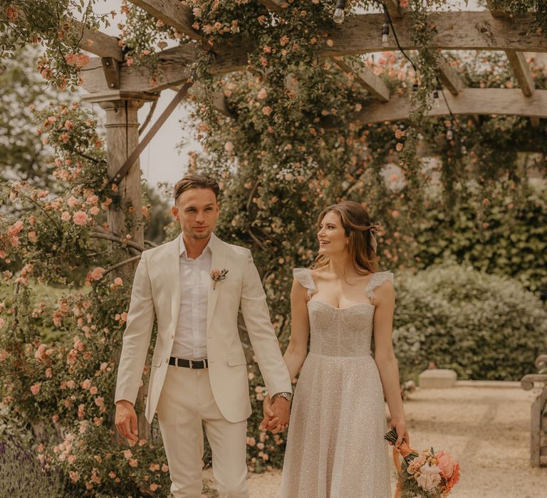 Bride in a sparkly Made With Love dress holding hands with her groom in a stone coloured suit 