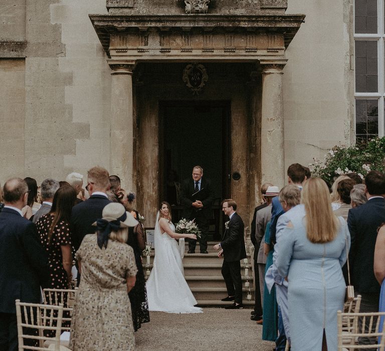 Bride & groom stand in large doorway for outdoor ceremony at Elmore Court 