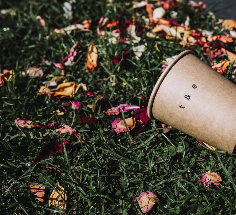 Hand pressed brown cup with initials next to dried confetti on grass