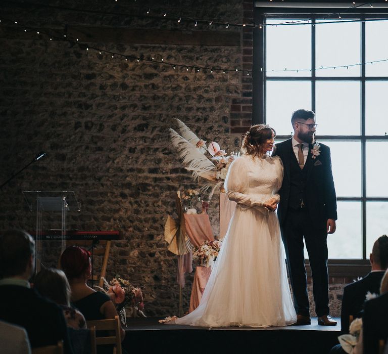 Bride & groom stand in front of large window on their wedding day