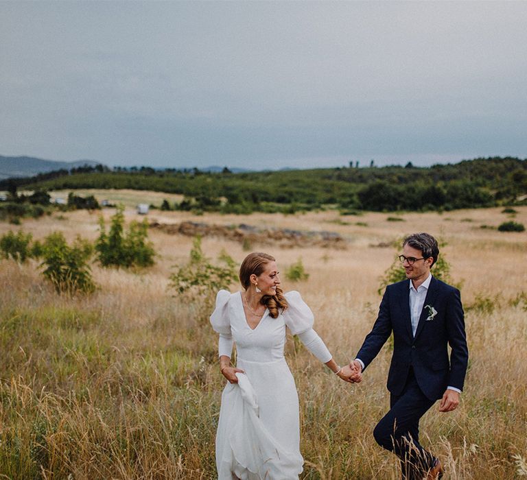 Bride & groom hold hands through golden fields in Croatia