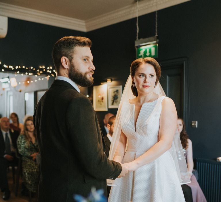 Bride and groom hold hands during ceremony at town house venue in Norwich