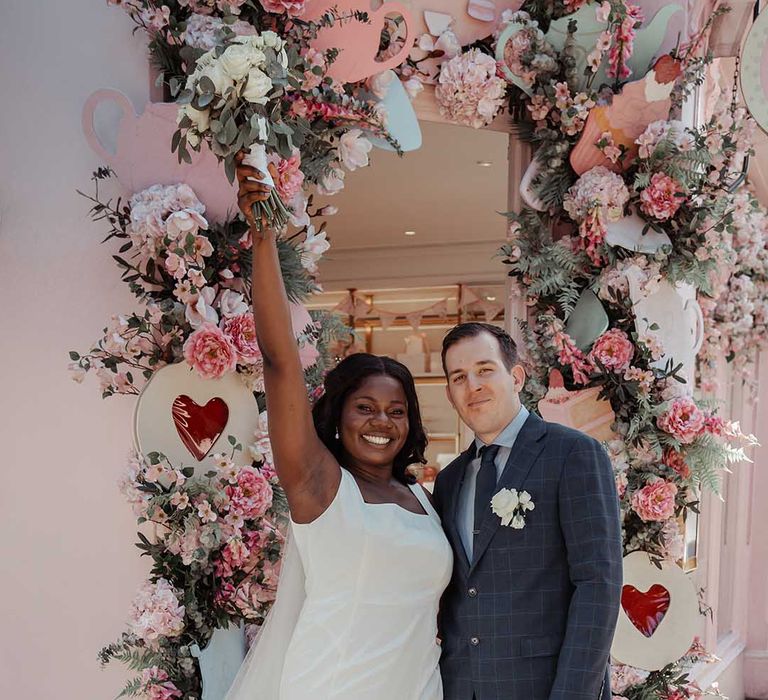 Bride & groom stand outside colourful floral archway in London on their wedding day after Chelsea Old Town Hall ceremony