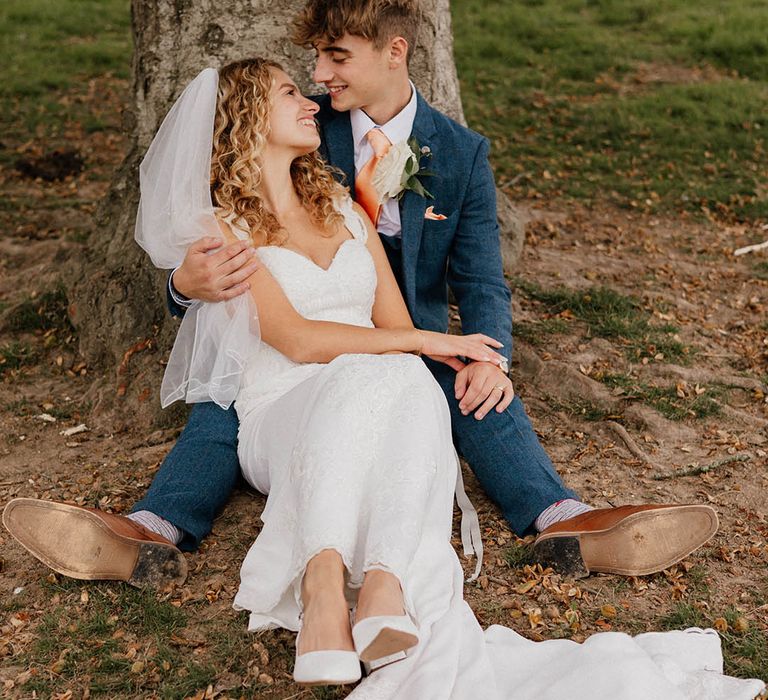 Bride & groom sit together outdoors as bride looks back toward groom on their wedding day