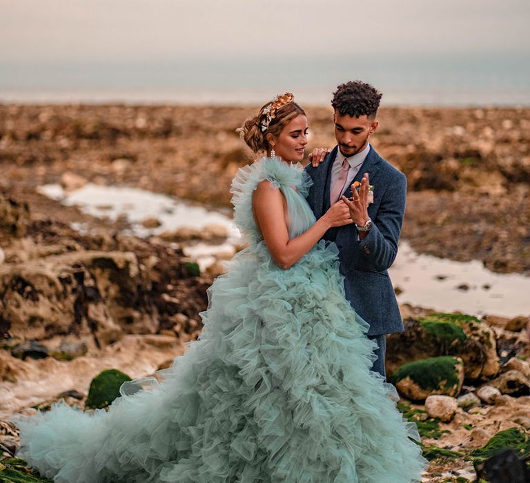 Bride in a Millia London coloured wedding dress with her groom in a blue wool suit on the beach 